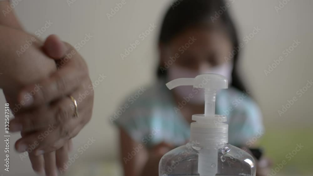 Mother cleaning her hands with alcohol gel and wearing protective mask before approach and combing her daughter's hair during COVID-19 outbreak situation. Coronavirus protection. Mother cleaning her hands with alcohol gel and wearing protective mask before approach and combing her daughter's hair during COVID-19 outbreak situation. Coronavirus protection.