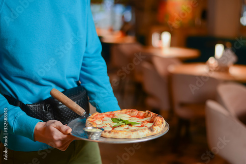 Waiter carrying plate with a tasty pizza. Pizza Margherita with cheese. Italian food. Italian restaurant.