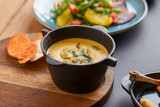 A bowl of spicy pumpkin soup with blue cheese served on a wooden board.