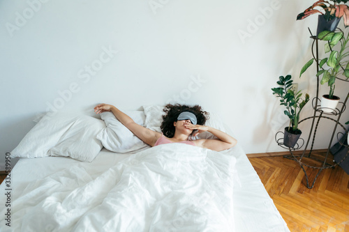 woman with sleeping mask in bed morning light through curtains
