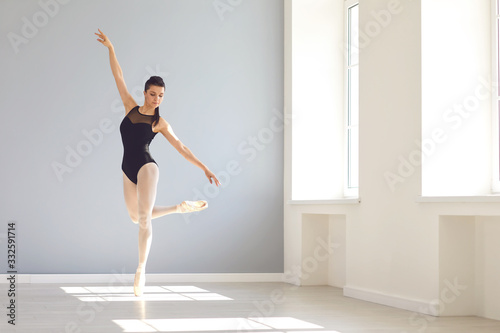 Ballerina posing in a bright class studio with windows.