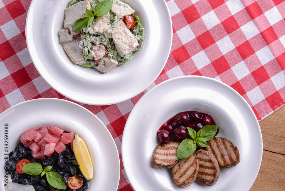 Grilled meat pieces with sauce, pasta with pesto, black pasta with salmon fish and lemon.