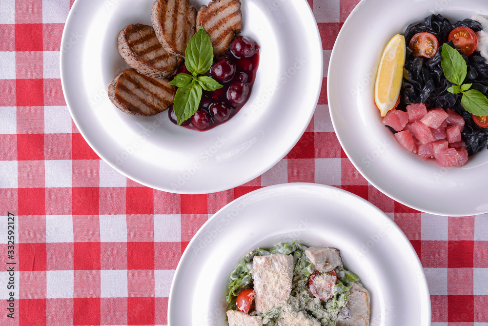 Grilled meat pieces with sauce, pasta with pesto, black pasta with salmon fish and lemon. Grilled meat pieces with sauce, pasta with pesto, black pasta with salmon fish and lemon.
