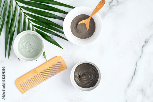 SPA facial clay mask in bowls and tropical palm leaf on marble background. Natural organic beauty products for face skin care and treatment. Flat lay  top view.
