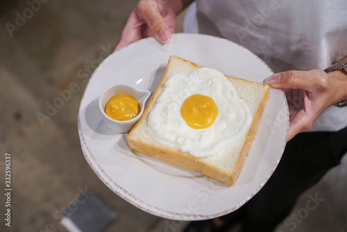 Fried Egg Toast. Woman holding a plate of sliced toast topped with fresh cream and salted egg lava cream sauce on wooden table.