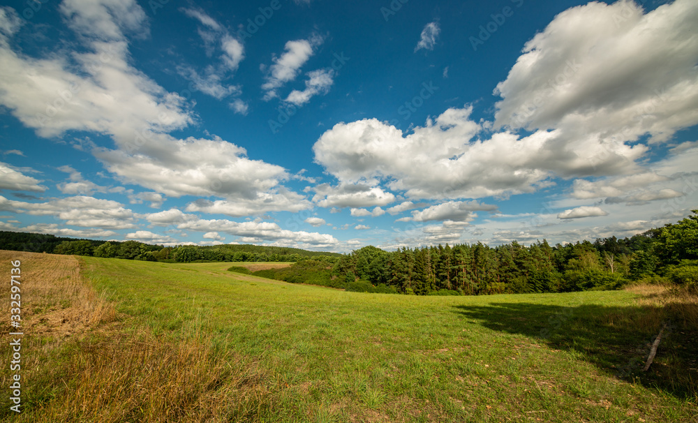 land view in small valley with field, meadow, forest and blue cloudy sky land view in small valley with field, meadow, forest and blue cloudy sky