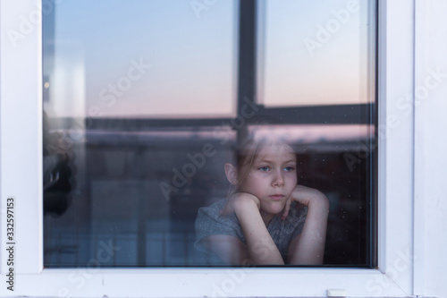 A sad, lonely child sits on the windowsill and looks out the window. Stay at home quarantine coronavirus prevention of the pandemic. The view from the street. Prevention of the epidemic. photo