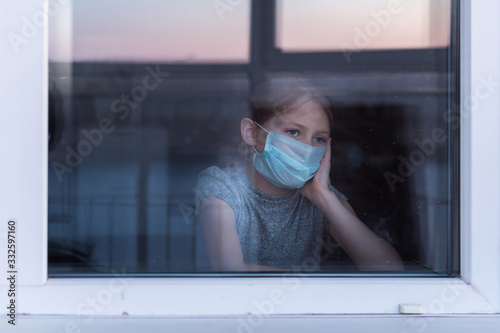 Stay at home quarantine coronavirus pandemic prevention. Sad child in protective medical mask looks out window. View from street. Prevention epidemic.