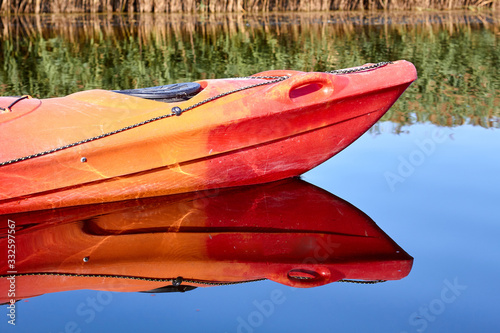 Prow of red tourist kayak on a calm river. Reflection of a kayak in the water