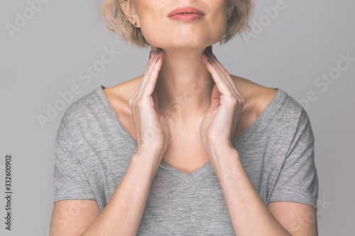 Female checking thyroid gland by herself. Close up of woman in white t- shirt touching neck with red spot. Thyroid disorder includes goiter, hyperthyroid, hypothyroid, tumor or cancer Health care. photo