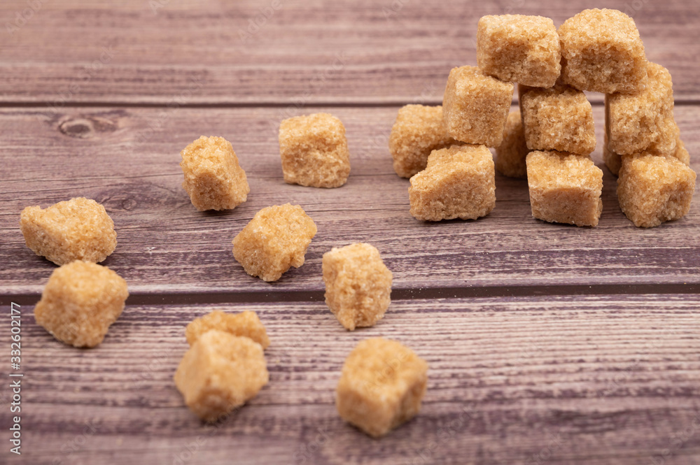 Pieces of brown cane sugar scattered on a wooden background. Close up. Pieces of brown cane sugar scattered on a wooden background. Close up.