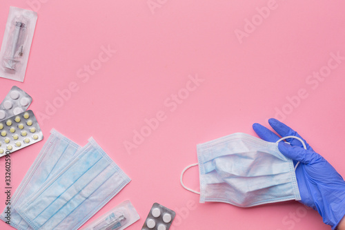 Medical protective masks, disposable syringes, pills and hand in latex glove on a pink background. The concept of protecting health from the virus. Copy space.