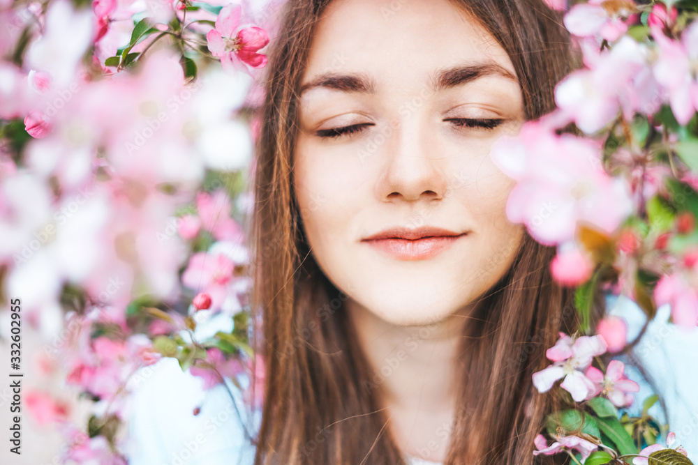 Young girl with closed eyes surrounded by flowers of a pink apple tree.