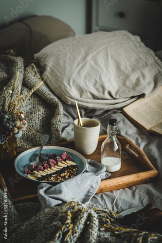 Breakfast in bed with cereals flakes or granola with nuts  dry fruits and raspberries on a white cozy bed with book and flowers.