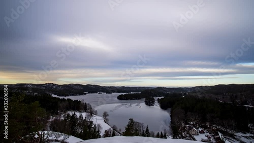 Time lapse shot of dark clouds above a lake, hills and forest, on a sunny, winter sunset, in Grimenes, Agder, South Norway photo