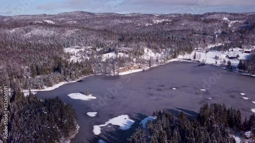 Aerial, drone shot overlooking a icy pond, hills and forest, on a sunny, winter day, in Risvann, Birkeland, Agder, South Norway photo