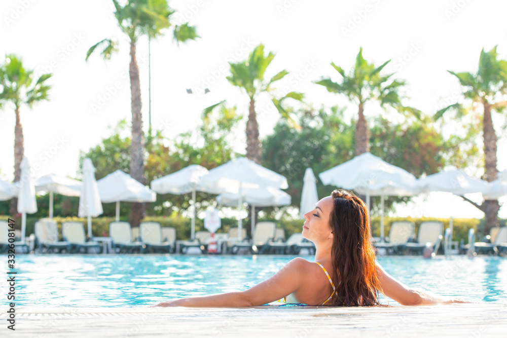 Beautiful young woman in the bathing suit girl is in the pool in a relaxed pose and sunbathes. Enjoying summer, relax. Vacation mood