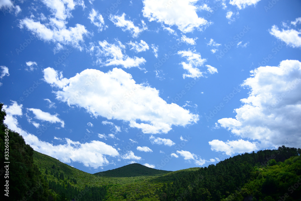 Paisaje de montes de bosques verdes y gran cielo azul con nubes blancas