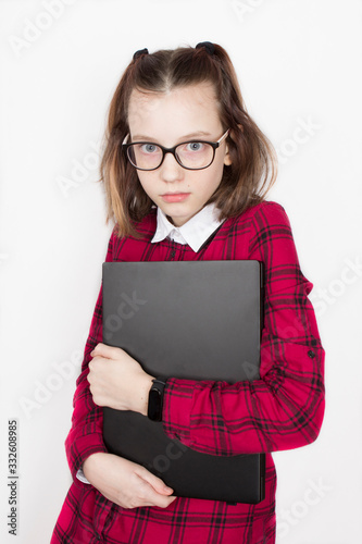 girl child wiseacre excellent pupil in glasses, in a red plaid shirt dress outfit and with a laptop in her hands photo