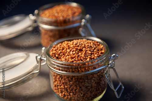 Buckwheat in a glass jar. Buckwheat grain stocks for porridge. Two cans on a table with buckwheat. Food  simple background  still life. Close-up. Place for text.