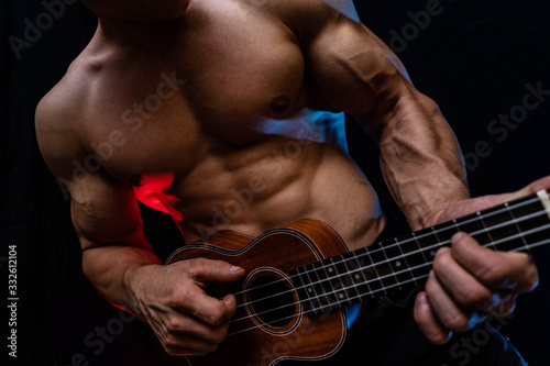 Muscular man with naked torso with ukulele and smoked colorful background 