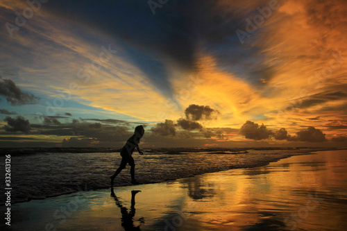 Silhouette boys play on the beach alone at dusk with dramatic sunset sky.