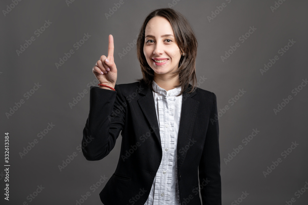 Portrait of wonderful young business woman with her finger up has come up with an idea, poseing on isolated gray background