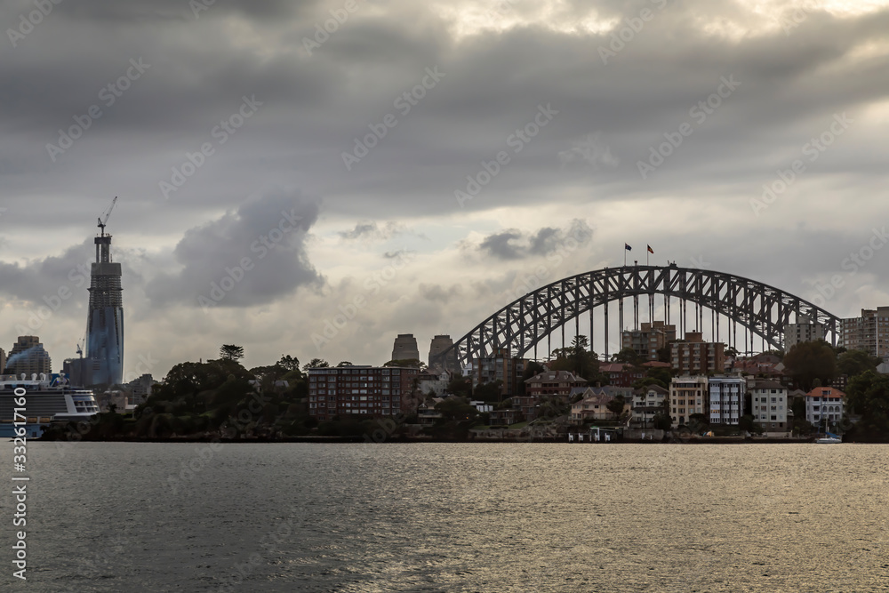Naklejka premium Sydney in Australia, the skyline with the Harbour Bridge during a cloudy but warm day in summer.