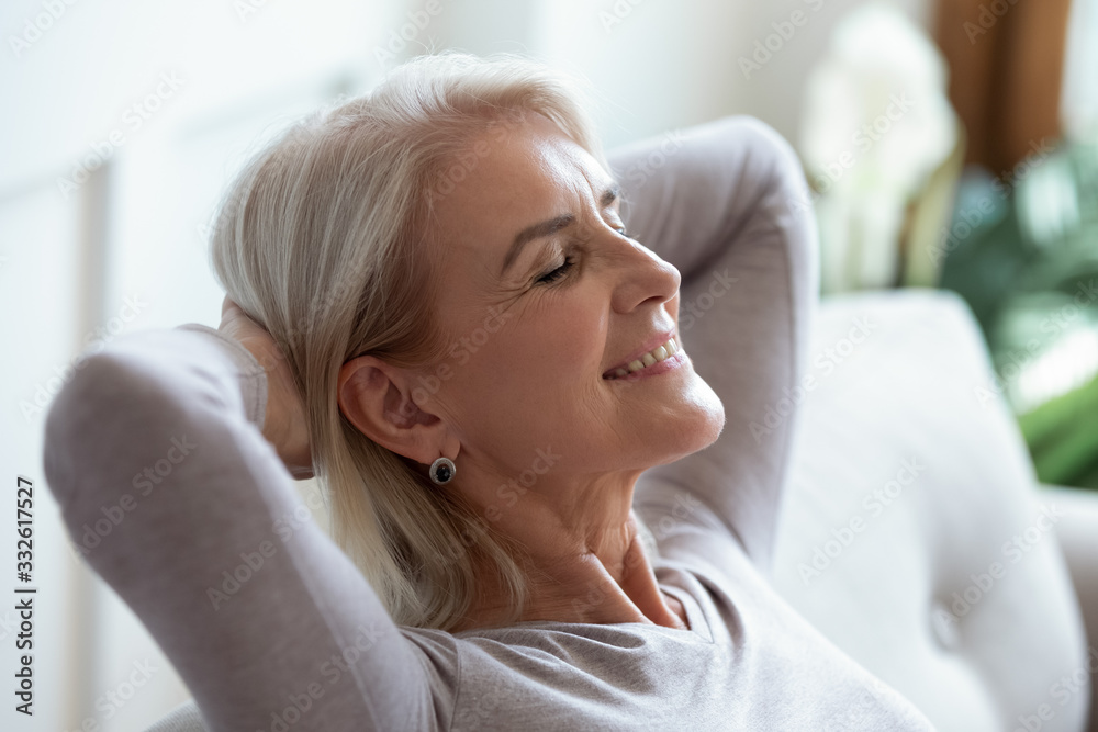 Smiling older woman relaxing with hands behind head on cozy sofa at home, happy sincere mature female with grey hair enjoying weekend, stretching on couch, resting and daydreaming, leaning back Smiling older woman relaxing with hands behind head on cozy sofa at home, happy sincere mature female with grey hair enjoying weekend, stretching on couch, resting and daydreaming, leaning back