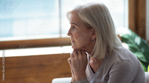 Profile unhappy upset older woman sitting alone and thinking about problems, feeling lonely, suffering from depression, dementia or mental disorder, frustrated mature female looking in distance