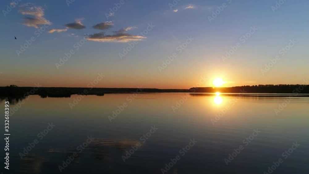 Orange fire sunset on a clear warm summer evening is reflected in a lake or river. Flying over the deep blue water surface. Orange fire sunset on a clear warm summer evening is reflected in a lake or river. Flying over the deep blue water surface.