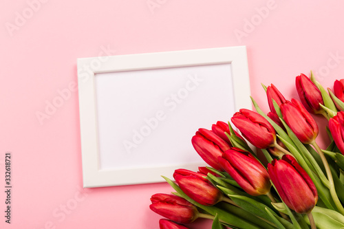 White photo frame as a template with a bouquet of red tulips on a pink background. Beautiful festive vertical blank for congratulation text or certificate.