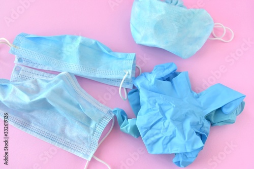 Used blue surgical protective masks and gloves. Medical trash. Used Coronavirus protection equipment on pink background. Used face masks and sterile glove. Covid-19. 