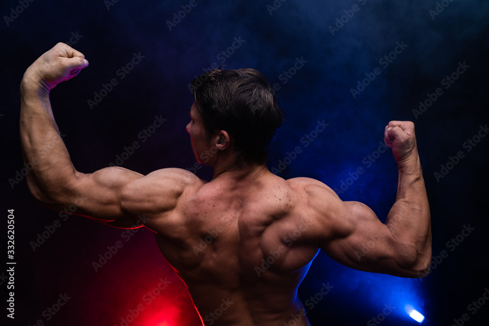 Muscular man showing muscles isolated on the black background with colored smoke. Concept of healthy lifestyle Muscular man showing muscles isolated on the black background with colored smoke. Concept of healthy lifestyle