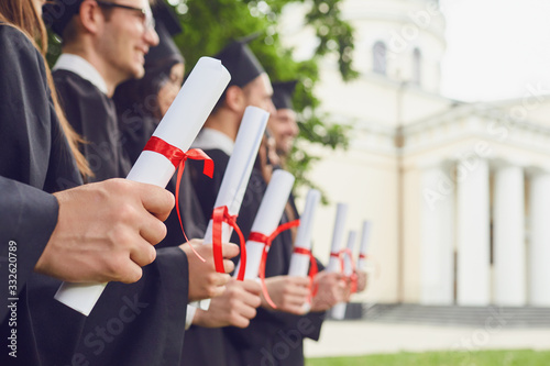 Scrolls of diplomas in the hands of a group of graduates.