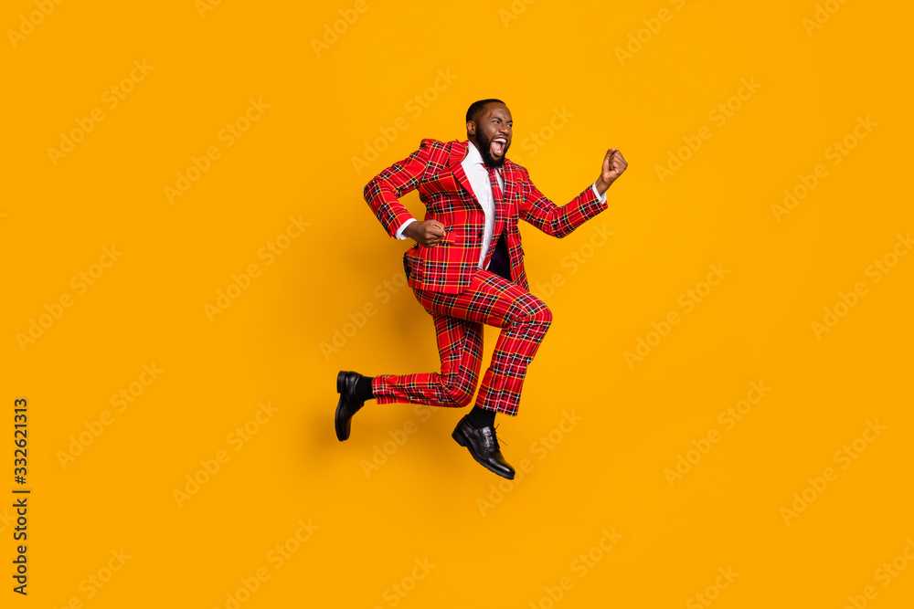 Full body profile photo of crazy dark skin guy jump high up celebrate achievement scream loud wear plaid red costume blazer pants shoes isolated bright yellow color background