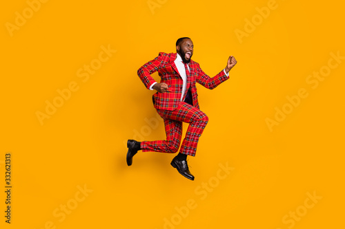Full body profile photo of crazy dark skin guy jump high up celebrate achievement scream loud wear plaid red costume blazer pants shoes isolated bright yellow color background