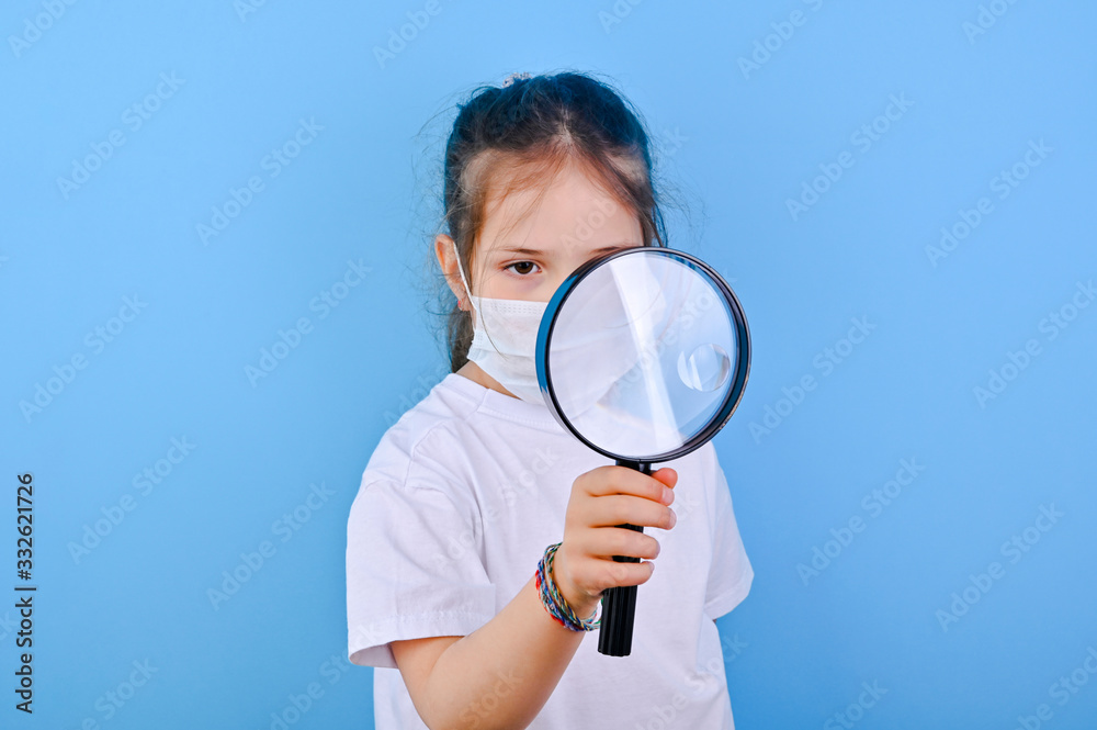 Baby in coronavirus. World pandemic concept COVID 19. Little girl in a protective medical mask is considering something. The emotions of the child in the photo. Copy space and blu background Baby in coronavirus. World pandemic concept COVID 19. Little girl in a protective medical mask is considering something. The emotions of the child in the photo. Copy space and blu background