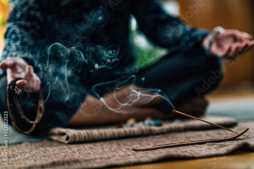 Mindful Woman Meditating with Burning Incense Sticks, Sitting in Lotus Pose. Hands in Lap, Palms Facing Upwards