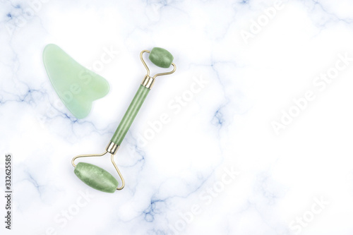Fototapeta Naklejka Na Ścianę i Meble -  Green face roller and gua sha massager made from natural jade nephritis stone over marble background.