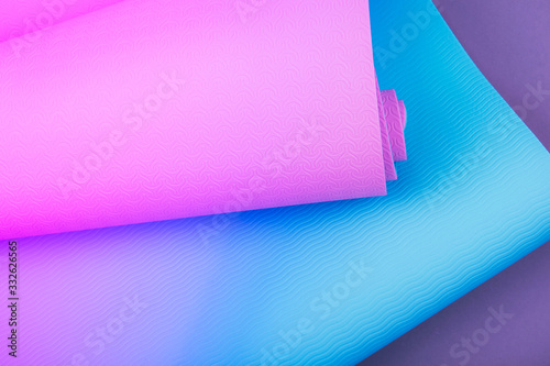 Top view of neon colored blue pink yoga mat on violet background. Space for text.