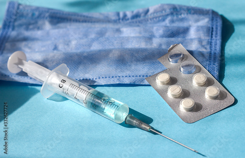 Medical mask, syringe and pills on a blue background with hard shadows from the sun, the concept of the pneumonia coronovirus influenza virus, treatment of the disease and quarantine