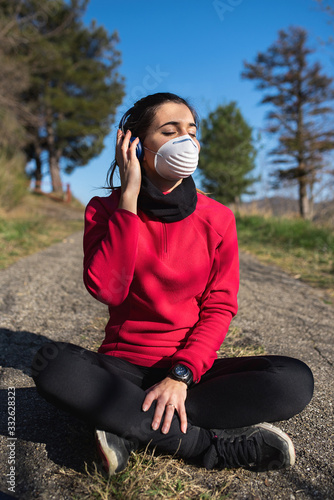 sitting woman listening to the music outdoor with headphones wearing a mask photo