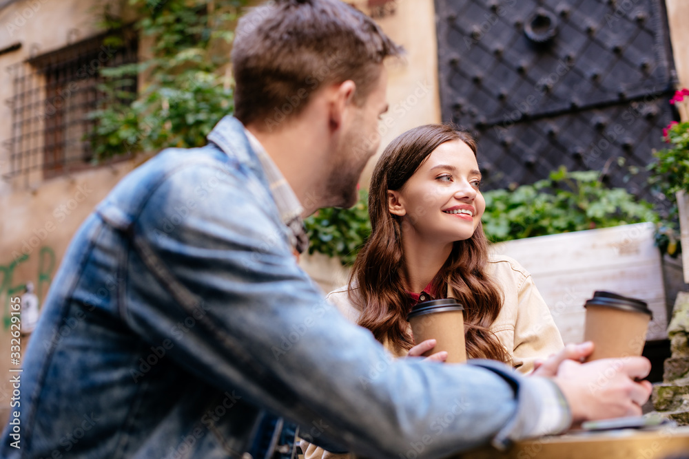 Selective focus of couple with disposable cups of coffee in cafe in city