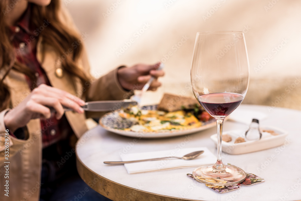 Partial view of woman eating with glass of wine in cafe