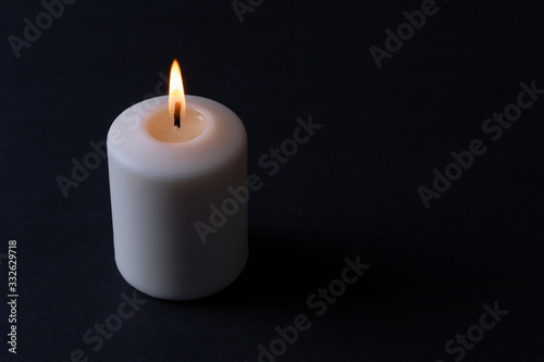 a thick white candle lit with an orange-red flame burning on a black background