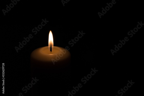 an orange-red flame of a candle burning on a black background, just top fragment of a candle seen
