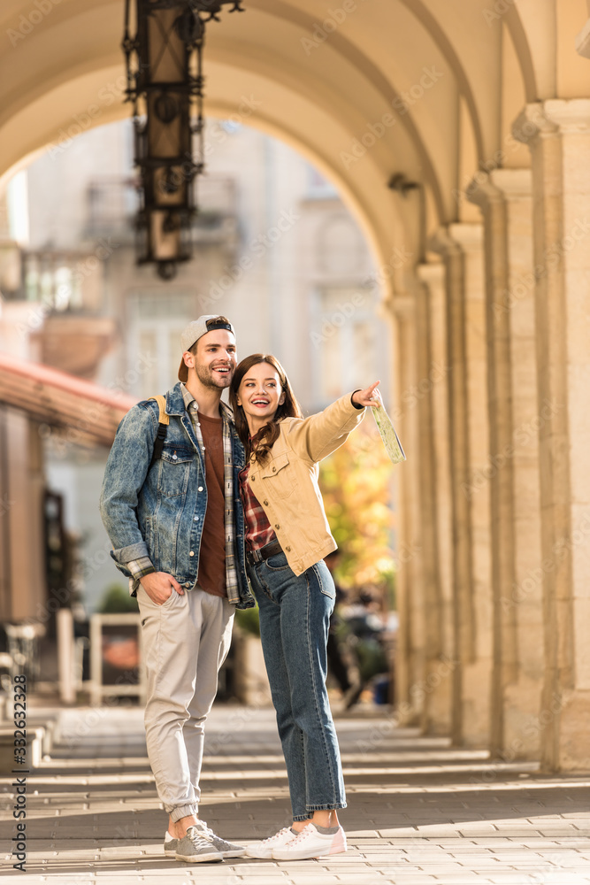 Selective focus of boyfriend and girlfriend pointing with finger and smiling in city