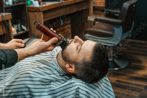 Beauty shop for men. Shaving a beard in a barbershop. Barber cuts his beard with a razor and clipper. close up Brutal haircuts. Hairdresser equipment. Selective focus.