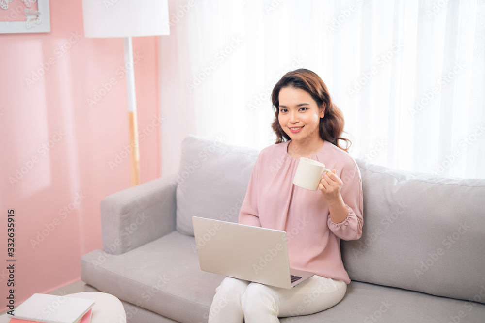 Charming Asian woman drinking coffee and using laptop when sitting on couch. Charming Asian woman drinking coffee and using laptop when sitting on couch.